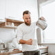 Man stands in kitchen pouring hot water into a mug to make an instant latte.