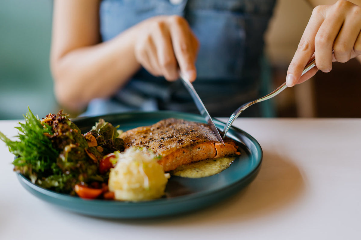 Woman cuts salmon as part of a protein-rich superfood plate.