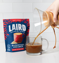 Sweet and Creamy Creamer Bag behind clear coffee mug with coffee being poured into it.