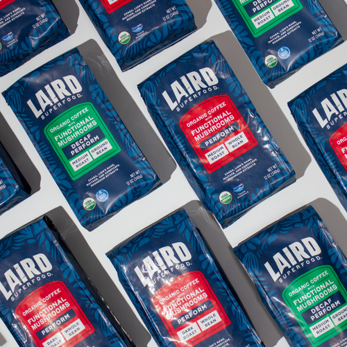 Multiple bags of Laird Superfood organic coffee with functional mushrooms, showing decaf and perform variations in blue packaging with red and green labels.
