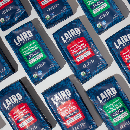 Multiple bags of Laird Superfood organic coffee with functional mushrooms, showing decaf and perform variations in blue packaging with red and green labels.