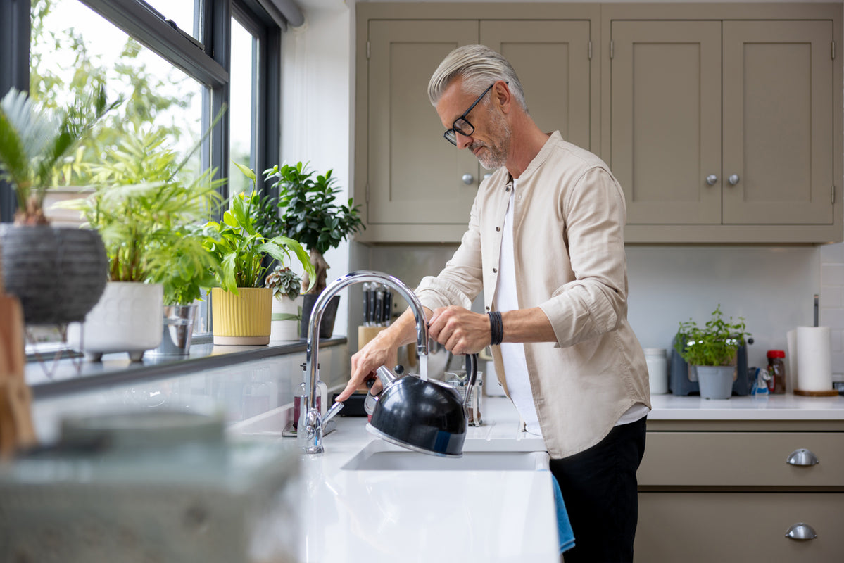 Man filling a kettle in his kitchen with tap water