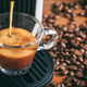 Espresso being brewed into a glass cup with coffee beans surrounding it