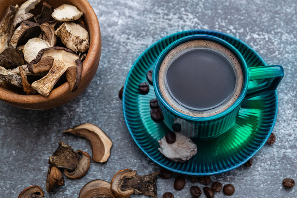 A cup of coffee next to a bowl of mushrooms illustrates the current trend of shroom coffee.