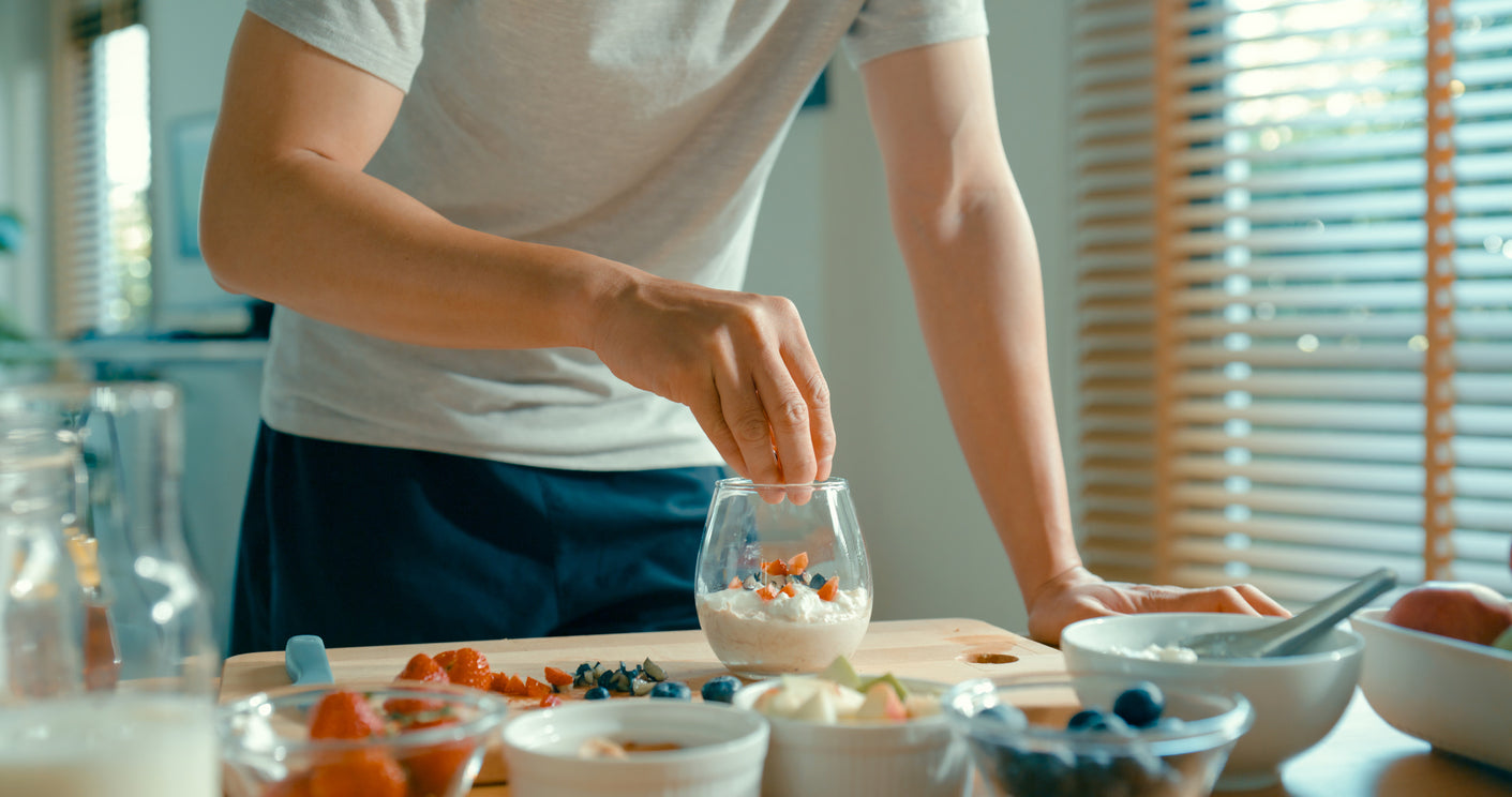 Man adds berries to a yogurt cup,  using various superfoods to make a healthy breakfast.