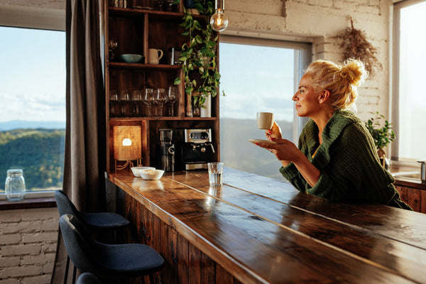 Middle-aged woman enjoys her morning cup of coffee at her kitchen bar, which may contribute to slower aging. 