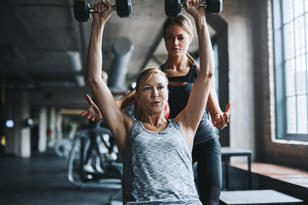 Middle-aged woman lifts weights with a trainer to boost energy.