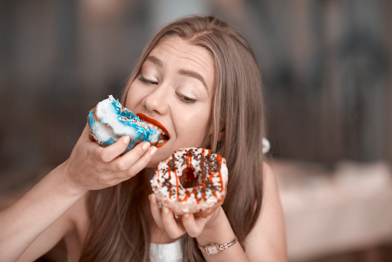 Woman eats two doughnuts illustrating that texture impacts our cravings and how much we eat.