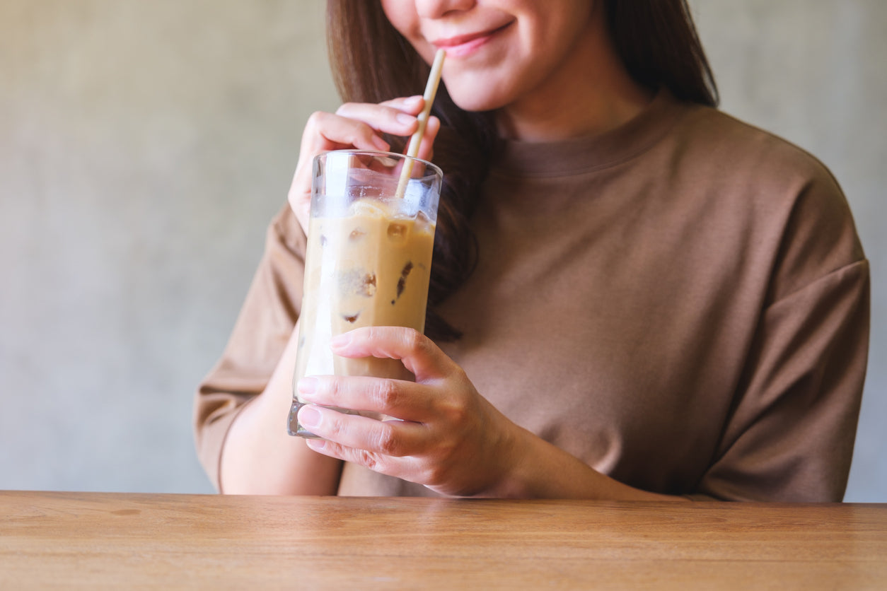 Woman sips iced coffee made with high-protein coffee creamer. 
