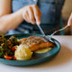 Woman cuts salmon as part of a protein-rich superfood plate. 