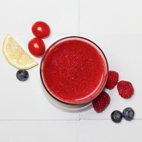 Antioxidant Daily Reds powder mixed in a clear glass, top down with raspberries, lemon, blueberries and cherry tomatoes surrounding the glass