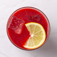 Antioxidant Daily Reds powder mixed in a clear glass with ice and a lemon wedge