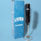 Black handheld battery powered frother with stand next to 'Laird Superfood' branding on a blue box with a light blue background