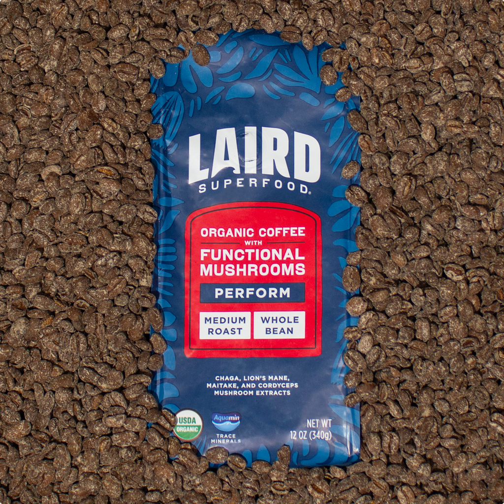 Laird Superfood  medium roast whole bean coffee with functional mushroom extracts in blue-red bag, 12 oz surrounded by the coffee beans.