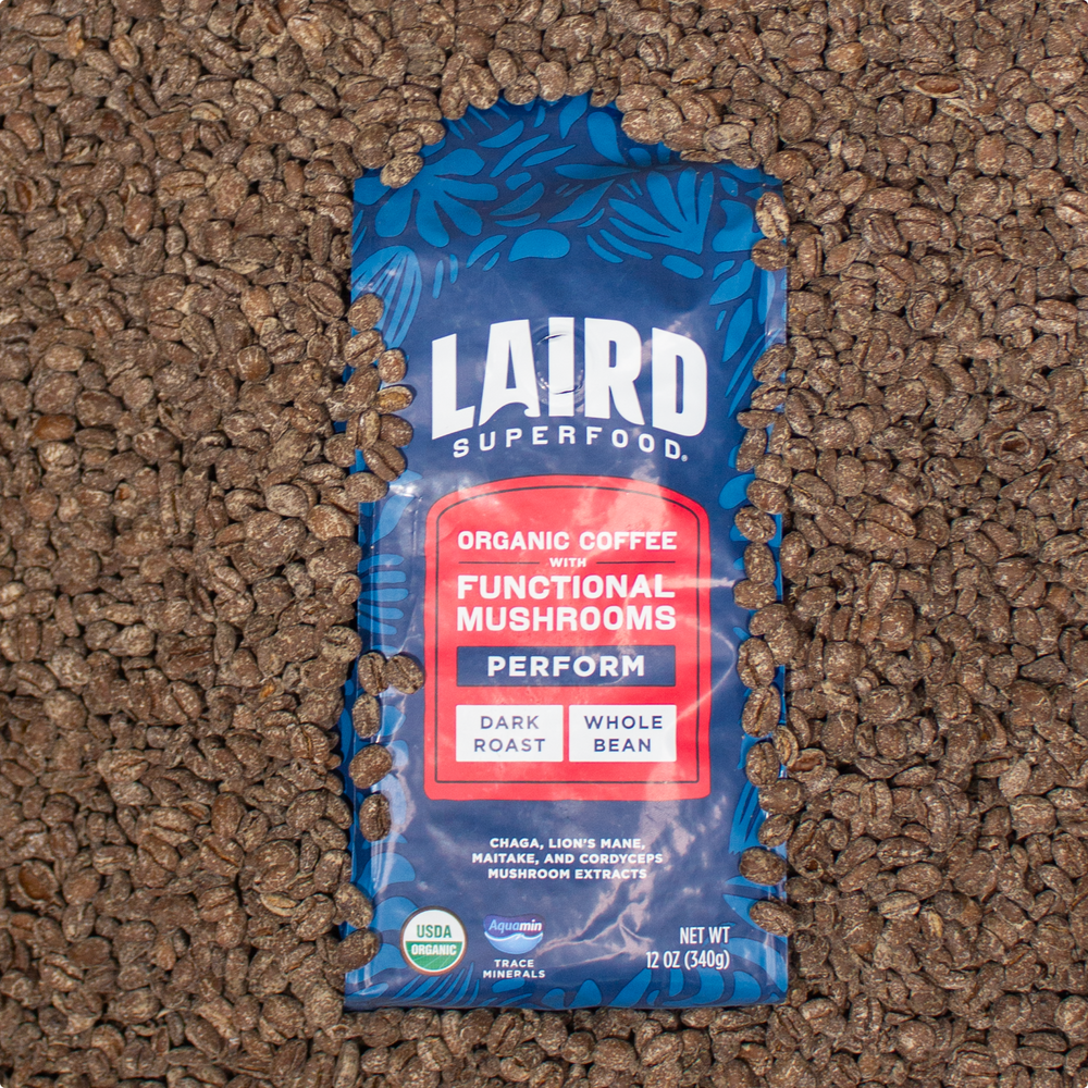 Laird Superfood  medium roast whole bean coffee with functional mushroom extracts in blue-red bag, 12 oz surrounded by the coffee beans.