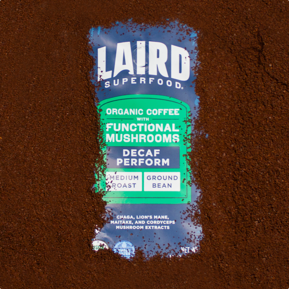 Bag of Laird Superfood organic decaf coffee with functional mushrooms, medium roast ground bean, surrounded by coffee grounds.