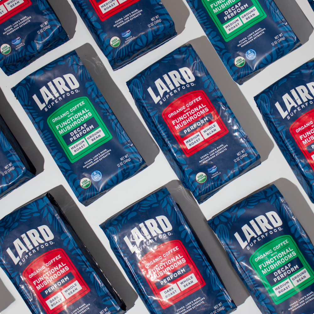 Multiple bags of Laird Superfood organic coffee with functional mushrooms, showing decaf and perform variations in blue packaging with red and green labels.