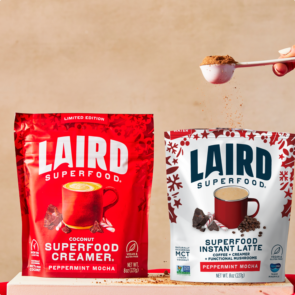 Two Laird Superfood packages, one red and one white, with a spoonful of powder above them on a beige background.
