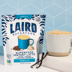 Laird Superfood Vanilla instant latte with a white glass mug filled with latte and vanilla bean next to it. 