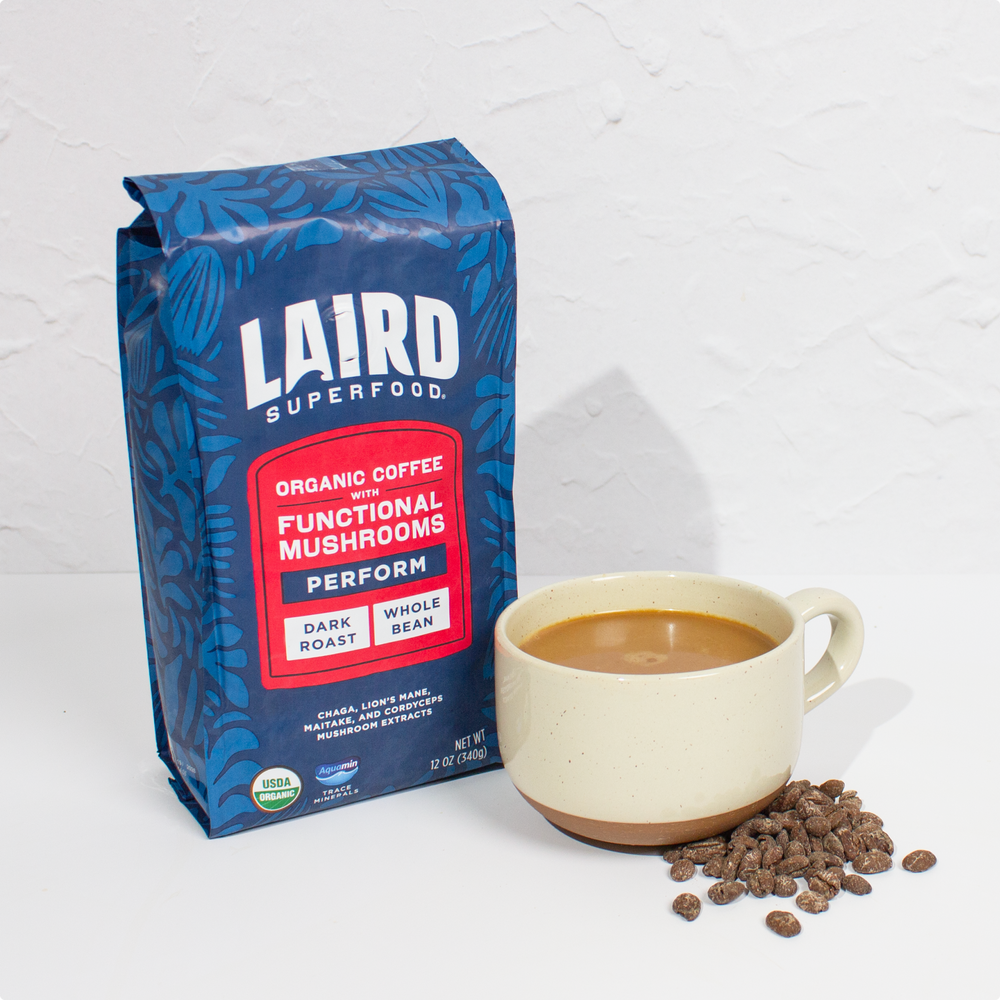 Bag of Laird Superfood organic dark roast whole bean coffee with functional mushrooms next to a cup of coffee and the coffee beans.