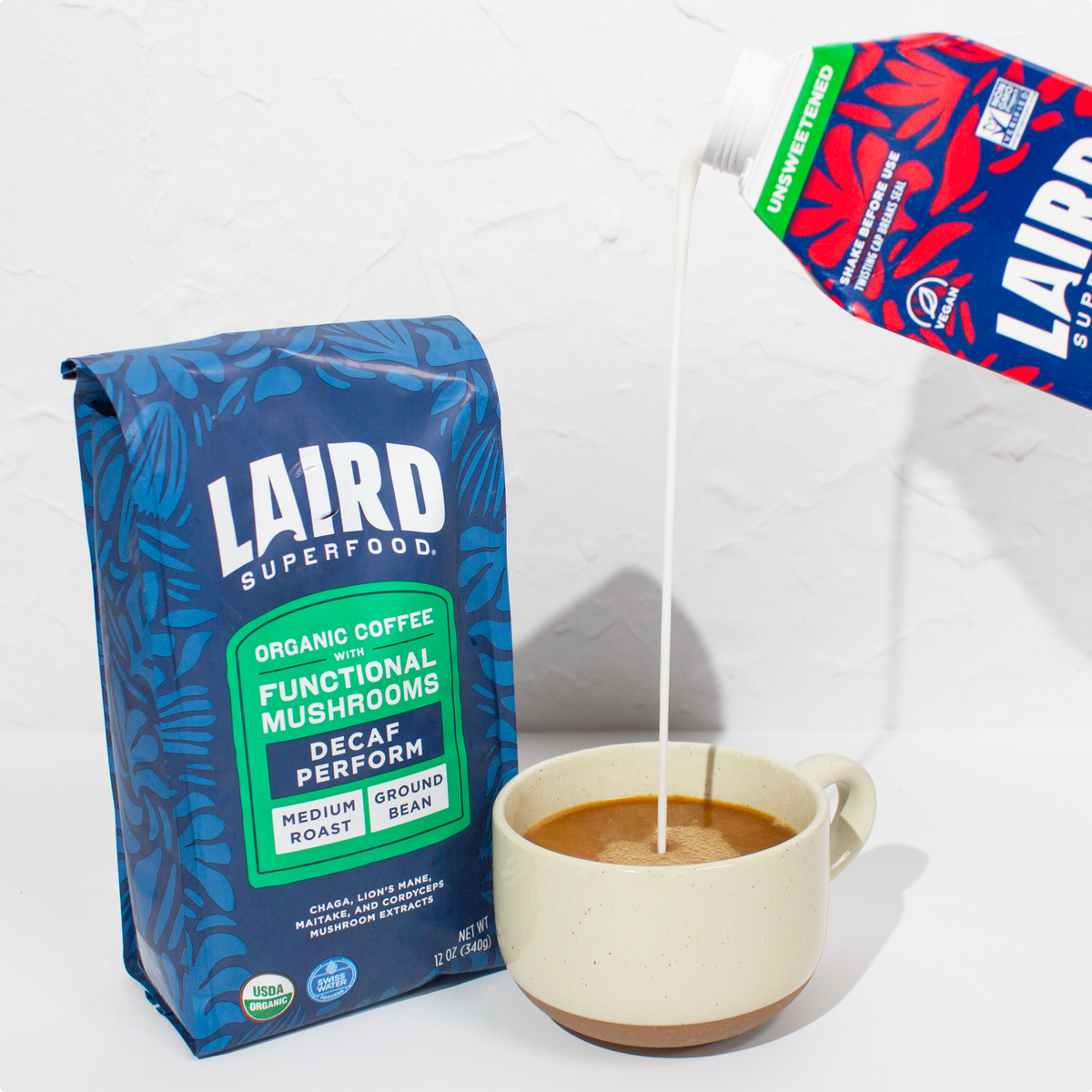 Bag of Laird Superfood organic decaf coffee with functional mushrooms next to a cup of coffee being poured with unsweetened creamer.