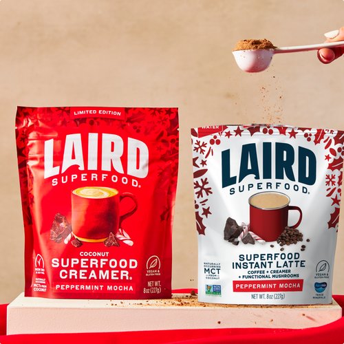 Two Laird Superfood packages, one red and one white, with a spoonful of powder above them on a beige background.