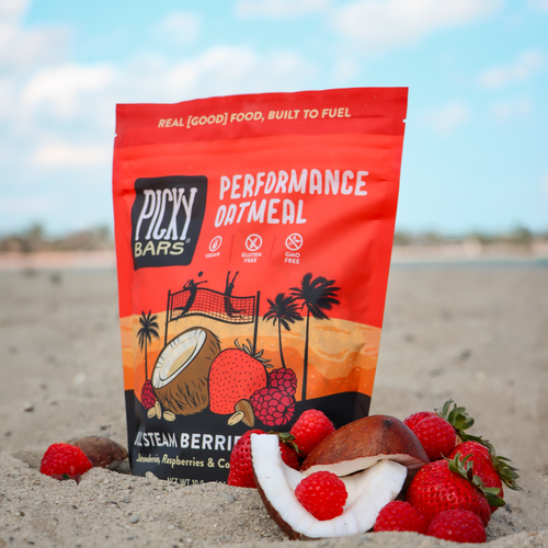 Picky Bar's Oatmeal with Berries and Cream in the sand on the beach with fresh strawberries and coconut pieces